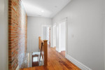 Modern second-floor apartment hallway featuring hardwood floors and exposed brick wall