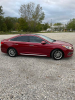 2015 Hyundai Sonata Limited in red, parked on gravel with trees in the background, showcasing its sleek design.