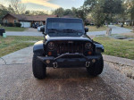 Front view of a 2012 Jeep Wrangler Sahara 4WD in dark green, showcasing lifted tires and aftermarket accessories.