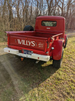 1951 Willy's Jeep pickup truck in red, showcasing its classic design and rear view with four-wheel drive label.