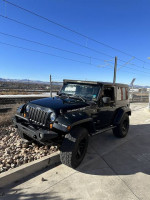 2007 Jeep Wrangler Rubicon in black with off-road tires parked near tracks, showcasing its rugged design.