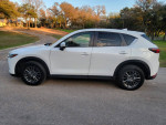 2019 Mazda CX-5 Touring in white, parked on a road, showcasing its sleek design and modern features.