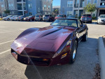 Beautiful burgundy 1980 Chevrolet Corvette parked in front of modern apartments, showcasing pristine condition.