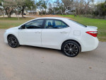 Side view of a 2016 Toyota Corolla S, white color, parked on a paved surface, showcasing its sleek design and alloy wheels.