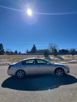 2005 Nissan Maxima parked under clear blue sky, showcasing its clean exterior and new tires.