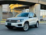 2015 Volkswagen Tiguan SE 4Motion AWD in silver, parked near a fence with city backdrop, showcasing its clean exterior.