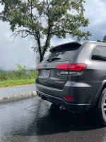 Rear view of a well-maintained Jeep Grand Cherokee Trailhawk, parked near trees on a rainy day.