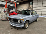 1972 BMW 2002 Tii project car in a garage, features include tan Recaro seats and disassembled engine.