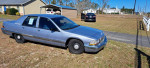 1995 Buick Roadmaster parked on grass, showcasing its classic body and chrome details with a clear blue sky.