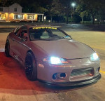 1995 Mitsubishi Eclipse GST with aftermarket parts showcasing its modified exterior and bright headlights at night.