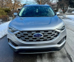Front view of a 2020 Ford Edge SEL FWD with a sleek silver exterior and shiny grille, parked in winter conditions.