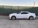 2017 Chevrolet Camaro ZL1 in white parked near a green fence, showcasing its sleek design and stylish wheels.