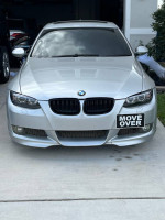 09 BMW 335i in silver with custom modifications and 'MOVE OVER' sign on front, parked in driveway.