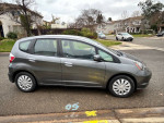 Side view of a 2013 Honda Fit in grey with low mileage, parked on a residential street.
