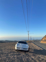 1987 Chevrolet Corvette parked on a scenic road with ocean view under a clear blue sky