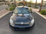 Front view of a black 2016 Volkswagen Beetle coupe parked under palm trees, showcasing its stylish design.