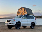 2008 Lexus GX 470 4WD in pearl white with rooftop tent parked by a scenic waterfront.