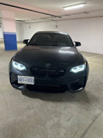 Front view of a 2018 BMW M2 F87 in a parking garage with headlights on.