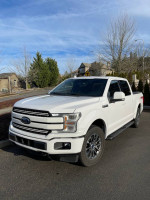 2018 Ford F150 Lariat FX4 white pickup truck parked on the street with sunny sky.