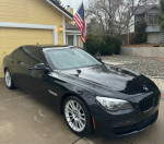 2013 BMW 750Li xDrive M Sport in black, showing sleek design and luxury features, parked in front of a yellow house.