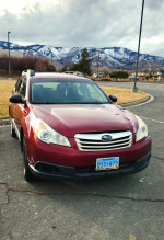 2012 Subaru Outback 2.5i AWD in red, parked outdoors with mountains in the background