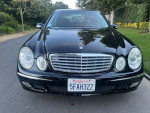 2004 Mercedes-Benz E320 luxury sedan in black with leather interior, showcasing front view on a scenic street.