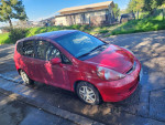 2007 Honda Fit in red parked on the street, featuring a manual transmission and good gas mileage.