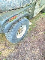 Close-up of a Jeep tire, showcasing wear and natural growth on a 1978 CJ 7 model needing extensive repair.