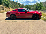 2014 Ruby Red Ford Mustang V6 RWD parked on a scenic road with custom striping and black wheels.