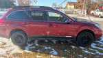 2012 Subaru Outback Limited in maroon color with black rims, parked on snow-covered grass.