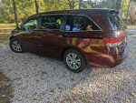 2016 Honda Odyssey SE minivan parked on gravel, featuring a maroon color and well-maintained exterior.